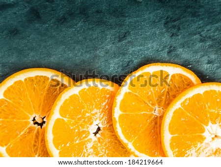 Colorful juicy fresh orange slices arranged as a lower border on textured slate with top corner vignetting and copyspace