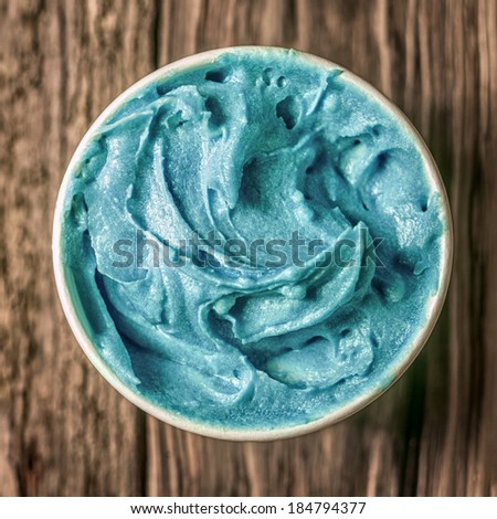 Cool refreshing turquoise blue ice cream in a takeaway tub standing on an old textured wooden table, overhead view in square format