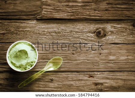 Takeaway tub of creamy green Italian ice cream with a plastic spoon on old rustic wooden boards with plenty of copyspace, overhead view