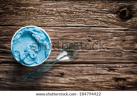 Cool refreshing blue Italian ice cream in a takeaway tub with a plastic spoon for a welcome treat on a hot summer day served on an old wooden table with copyspace, view from above