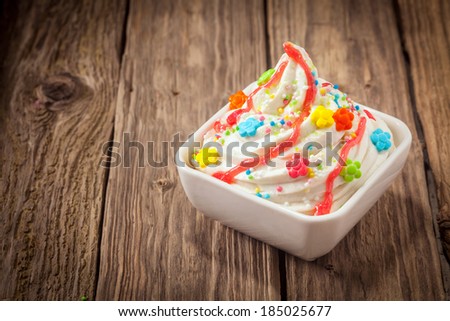 Colorful party ice cream dessert frozen yogurt with a swirl of vanilla ice cram topped with bright multicolored candy and sprinkles drizzled with syrup on an old textured wooden table with copyspace