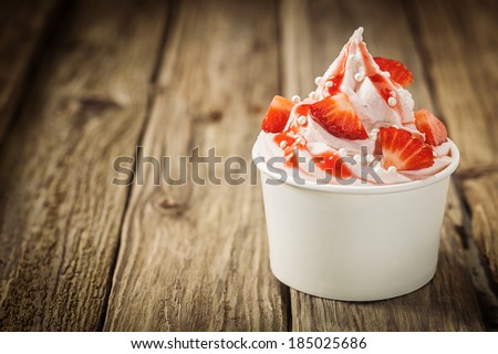 Ripe red tropical strawberries and vanilla ice frozen joghurt cream for a healthy refreshing cold summer dessert in a takeaway tub on an old rustic wooden table with copyspace