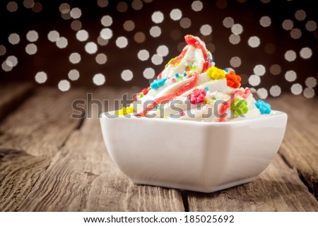 Colorful kids ice cream party dessert with a twirl of rich creamy vanilla ice cream topped with vibrant candy and sprinkles decorated with orange syrup with a bokeh of sparkling festive lights