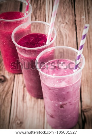 Healthy delicious trio of different berry smoothies with low fat yogurt arranged in a diagonal row, high angle view on an old rustic wooden background