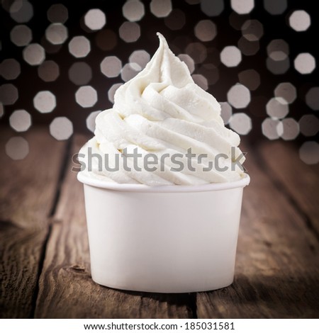 Tub of creamy vanilla or tangy lemon ice cream on an old wooden bar counter with a bokeh of festive party lights