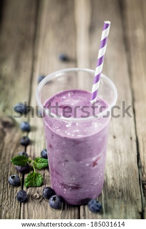 Glass of delicious purple healthy blueberry smoothie blended with ice cream or yogurt with fresh fruit on rustic wooden boards with copyspace