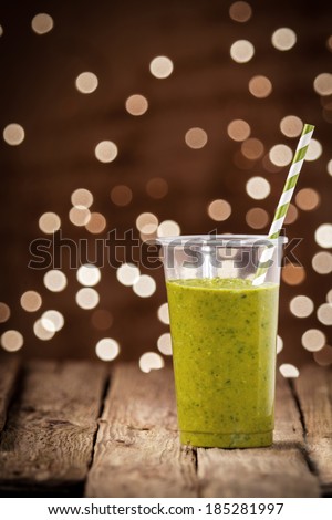 Healthy organic green vegetable and herb smoothie served on a rustic wooden table at a bar against a brown bokeh of twinkling lights with copyspace