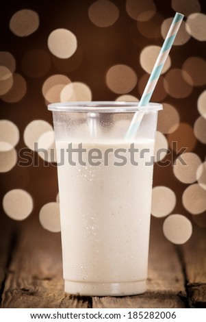 Creamy fruity smoothie on an old wooden bar counter against a festive brown bokeh of sparkling party lights at a summer celebration