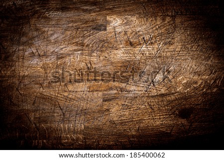 Background texture of old grungy scored wood with crisis-crossed cut marks from a knife and a heavy vignette