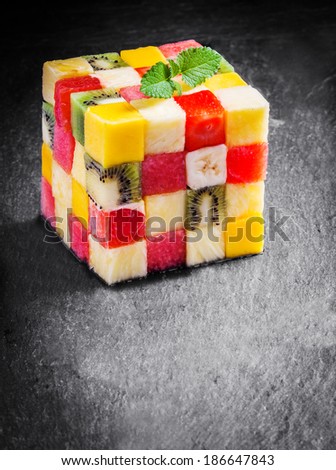 Colorful gourmet cube of diced fresh tropical fruit with watermelon, melon, orange, strawberry, banana, kiwifruit and apple garnished with mint on a slate kitchen counter with copyspace