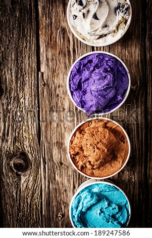 Gourmet selection of ice cream or frozen yoghurt in a variety of colours and flavours served on a rustic wooden table in a row of plastic takeaway tubs with copyspace