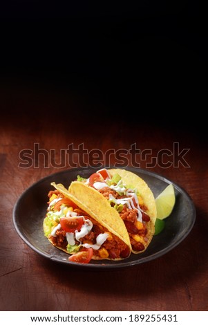 Mexican corn taco filled with spicy ground meat , salsa and salad served in a shallow wooden bowl on a wooden table with copyspace