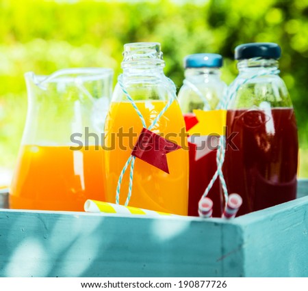 Homemade healthy freshly squeezed orange and berry juice in glass bottles and jugs standing in a wooden turquoise box on a table in a summer garden for a refreshing drink
