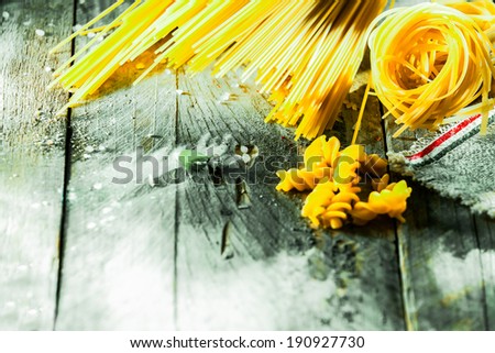 Variety of different Italian dried pasta ingredients arranged in the corner on rustic weather wooden boards with copyspace including spaghetti, fusilli , tagliatelli and linguini
