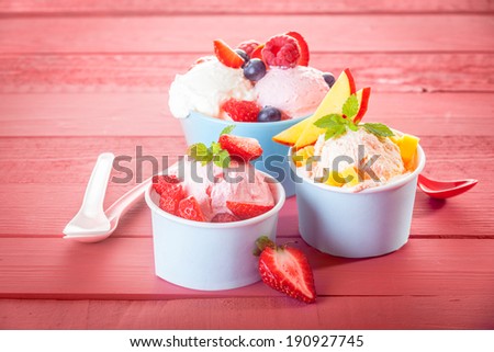Trio of individual servings of mixed fresh berries and tropical fruit with assorted ice cream flavors on a pink wooden background with copyspace for a summer treat