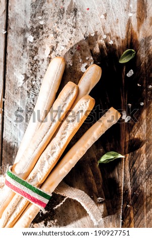 Italian grissini bread sticks made from crisp golden baked unleavened dough, tied in a bundle with a ribbon with the colors of the Italian national flag lying on a grunge rustic wooden table