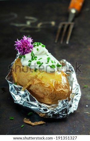 Foil baked jacket potato served in the aluminium foil wrapper topped with sour cream and fresh chopped chives and garnished with a purple chive flower
