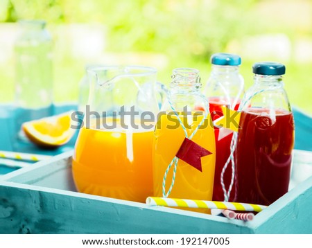 Healthy freshly squeezed fruit juice with bottles of orange citrus blend and fresh berry juice standing on a turquoise picnic table in a summer garden