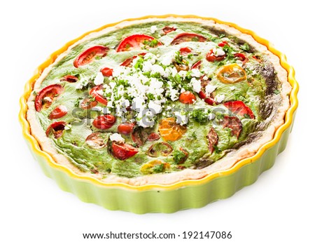 Savory egg, herb, tomato and cheese vegetarian quiche in a pastry crust served in a fluted pie dish on a white background