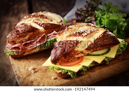 Lye bread rolls , a German and Bavarian speciality bread glazed and baked with lye, with cheese and salami with fresh lettuce, tomato and cucumber on an old wooden board