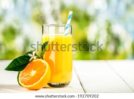 Tall glass of tasty freshly squeezed orange juice standing on an outdoor wooden picnic table on a hot summer day with a halved fresh orange