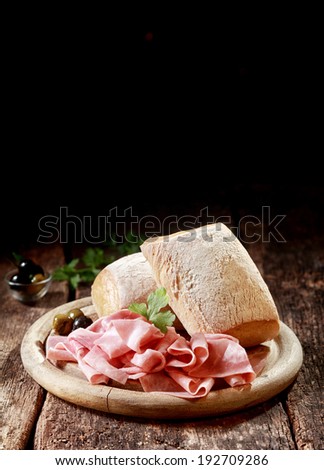 Cured thinly sliced German ham with crusty rolls for a country lunch served on a wooden platter with copyspace, vertical format