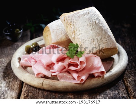 Country lunch with thinly sliced cured Bavarian ham and crusty rolls served on a wooden platter on a rustic wooden table