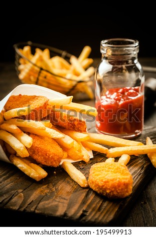 Fried golden crumbed fish fillets and French fries served in a paper cone with a tomato based sauce or dip on an old grunge wooden table in a fish shop