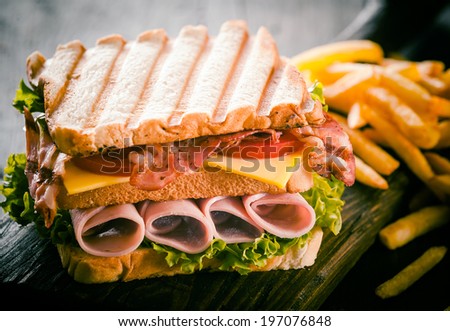 Toasted or grilled ham and cheese club sandwich with fresh lettuce and tomato and a side serving of potato chips, close up view