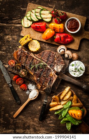 Wholesome spread with t-bone or porterhouse steak served with an assortment of healthy roasted vegetables and savory dips on a rustic wooden table in a country kitchen