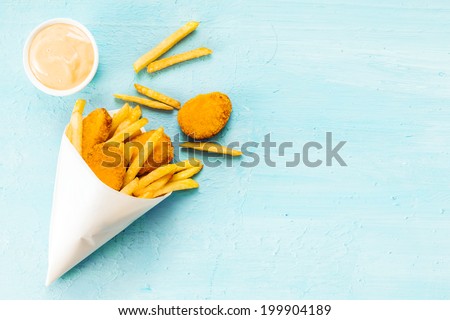 Overhead view on a blue background with copyspace of medallions of fried fish and chips in a takeaway paper cone with savory mayonnaise dip