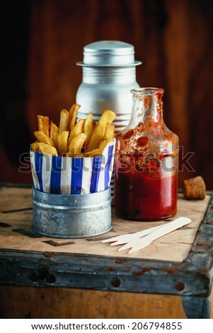 Colorful blue striped packet of crispy of French fries standing on a rustic wooden table in a fish and chip shop with condiments
