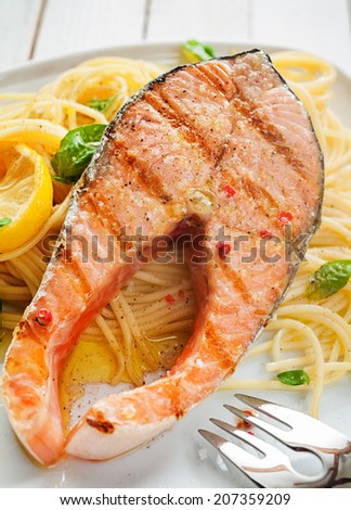 Seafood dinner of a gourmet grilled salmon cutlet steak on Italian linguine pasta seasoned with fresh basil and garnished with lemon