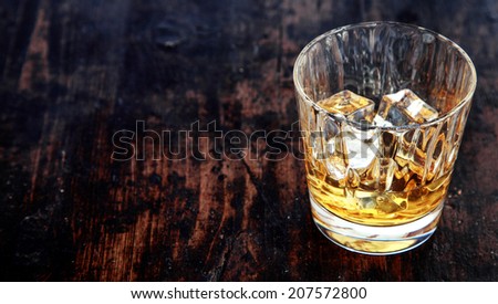 Close-up of a glass of whiskey, bourbon or scotch, with ice cubes, on an old rustic wooden table