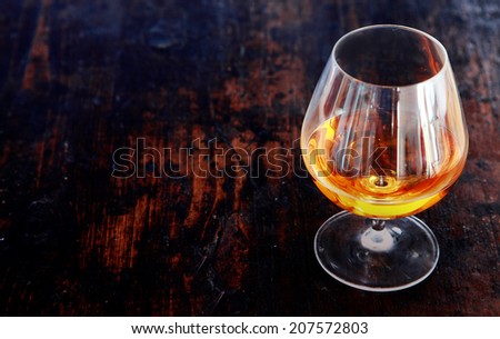 Glowing cognac or brandy in an elegant snifter glass on an old dark wooden bar counter with copyspace, high angle view