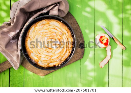 Delicious golden home baked apple pie viewed from above in an oven dish on a green wooden garden table in dappled sunlight for a relaxing summer meal and dessert