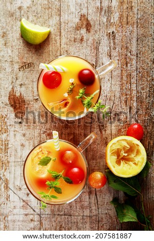 Glasses of fresh summer fruit cocktail with blended fruit juices garnished with fresh cranberries and herbs on a rustic wooden table, overhead view