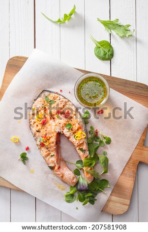 Succulent grilled salmon steak or cutlet seasoned with fresh spices and herbs with basil, rocket and olive oil dressing , viewed from above on a wooden board