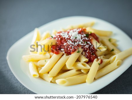 Serving of traditional cooked penne rigate pasta topped with a spicy tomato sauce topped with grated parmesan cheese