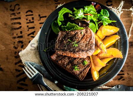 Overhead view of delicious,grilled beef steak with roasted pumpkin and fresh green herb salad on an old wooden packing case with printed text