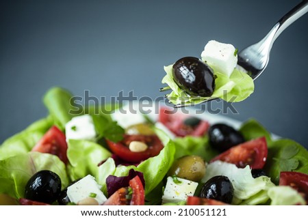 Enjoying a healthy Greek salad of feta cheese, olives tomatoes and leafy green with a fork suspended above the plate with lettuce, feta and olive on it