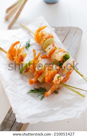 Two delicious gourmet seafood kebabs with pink prawns , fresh herbs and lemon on a crumpled sheet of white paper