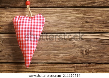 Handmade rustic hanging red and white checked heart ornament for Christmas or Valentines Day for a sweetheart or loved one with copyspace on a wooden background
