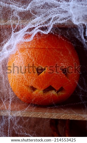 Spooky spider web covered jack-o-lantern formed from a fresh orange on a wooden shelf in a scary Halloween background