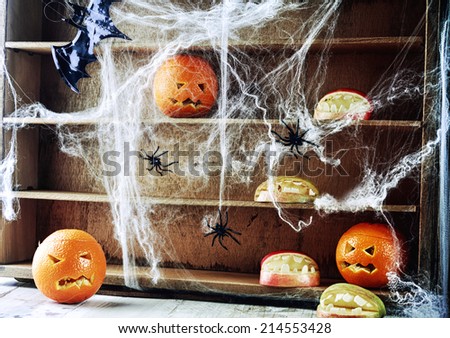 Spooky Halloween pantry with pumpkin lanterns and apples shaped as open mouths with teeth on wooden shelves draped in spider webs crawling with large black spiders