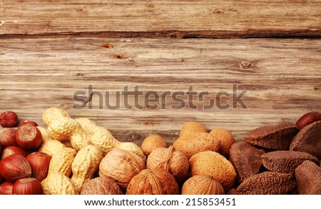 Border of assorted whole nuts in their shells including almonds, hazelnuts, brazil nuts, peanuts and walnuts on textured rustic wood with copyspace
