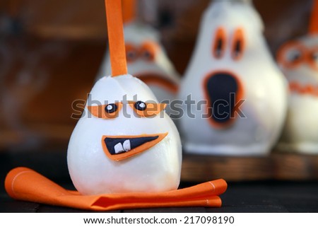 Fun edible Halloween pear desserts or treats for trick-or-treating decorated as ghosts and ghouls with a covering of white chocolate or marzipan with scary orange faces in different expressions