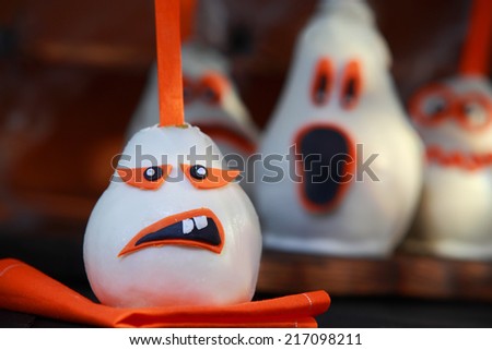 Creative edible Halloween decorations with pears coated in white chocolate or marzipan with a variety of scary ghostly faces and focus to one in front on a dark background