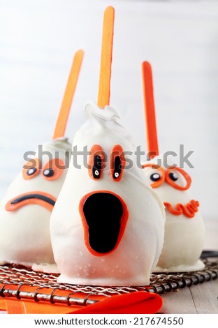 Edible homemade ghost Halloween dessert or party favors made from fresh pears coated in white chocolate and marzipan and decorated with a variety of scary expressions in orange with sucker sticks