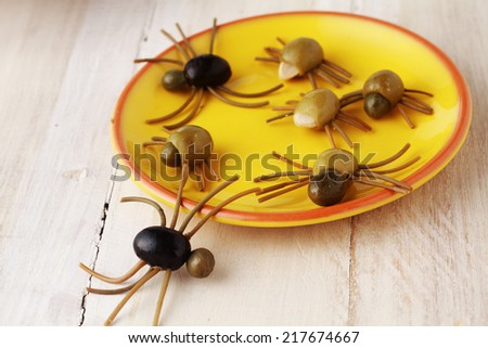 Creepy crawly Halloween spider snacks for a party celebration made from black and green olives with Italian spaghetti legs served on a yellow plate on a rustic white wooden table